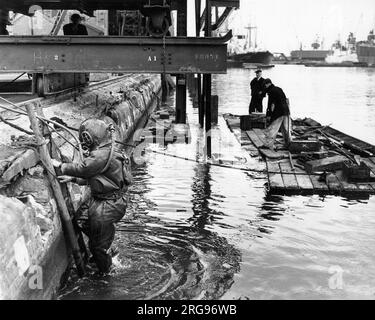 Dockside Szene mit zwei Männern auf einem Floß und einem Mann in einem schweren Taucheranzug auf der linken Seite, Fluss Themse, Hafen von London. Stockfoto