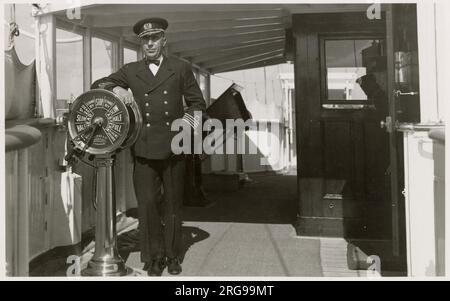 Captain der Royal Navy auf der Brücke eines Kriegsschiffs, lehnt sich an den Messingmaschinenraum Telegrafen auf volle Kraft voraus. Stockfoto