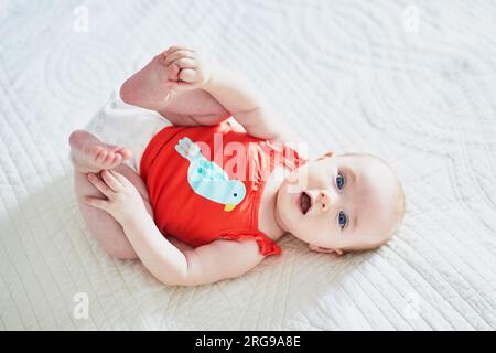 Süßes kleines Mädchen, das auf dem Rücken liegt und ihre Füße berührt. Glückliches, gesundes Kind im Kinderzimmer Stockfoto