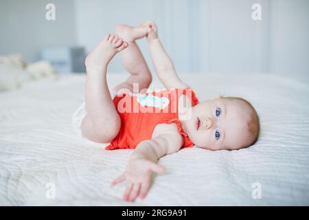 Süßes kleines Mädchen, das auf dem Rücken liegt und ihre Füße berührt. Glückliches, gesundes Kind im Kinderzimmer Stockfoto