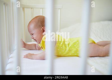 Ein bezauberndes Mädchen, das in einem Babybett lag, das an das Bett der Eltern angehängt war und weinte. Das kleine Kind will kein Nickerchen im Kinderbett. Säuglingskind im sonnigen Kinderzimmer Stockfoto