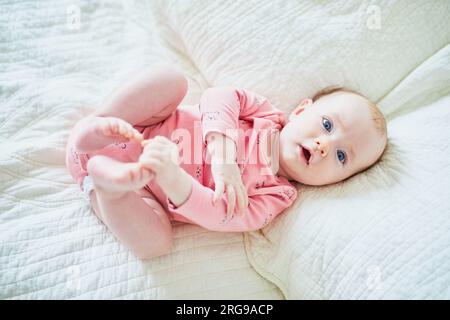 Ein bezauberndes, 4 Monate altes Mädchen, das auf dem Bett lag und ihre Zehen berührte Stockfoto