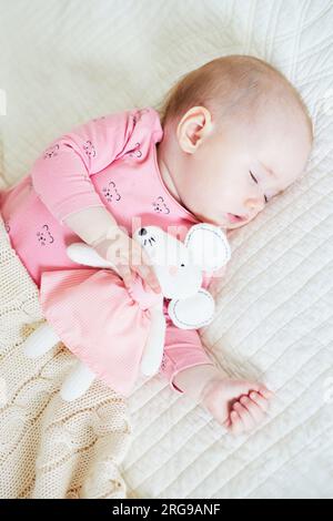 Ein kleines Mädchen schläft mit ihrem Lieblingsmaus. Kleines Kind schläft auf dem Bett mit Bettdecke. Das Schlaftrainingskonzept. Säuglingskind im sonnigen Kinderzimmer Stockfoto