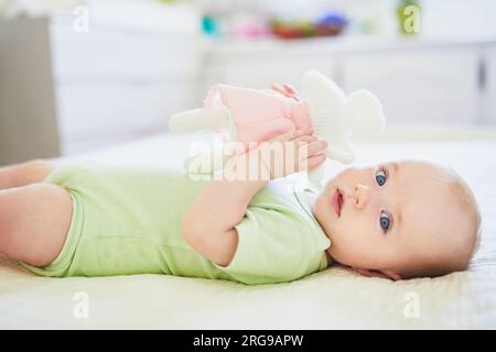 Süßes kleines Mädchen, das auf dem Rücken auf dem Bett liegt, mit weichem Spielzeug. Glückliches gesundes Kind zu Hause im Kinderzimmer Stockfoto