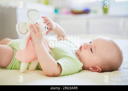 Süßes kleines Mädchen, das auf dem Rücken auf dem Bett liegt, mit weichem Spielzeug. Glückliches gesundes Kind zu Hause im Kinderzimmer Stockfoto