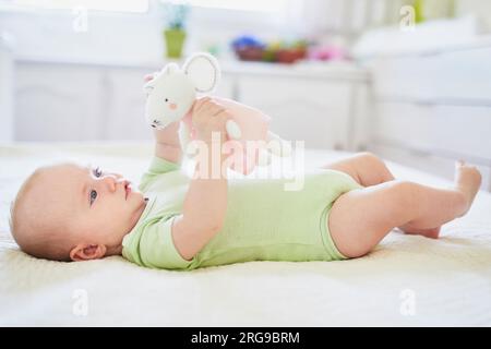 Süßes kleines Mädchen, das auf dem Rücken auf dem Bett liegt, mit weichem Spielzeug. Glückliches gesundes Kind zu Hause im Kinderzimmer Stockfoto