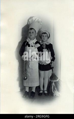 Zwei Kinder in schicken Kleidern; der kleine Junge ist als Koch gekleidet, während ein kleines Mädchen ein sehr respektables Dienstmädchen oder eine sehr respektable Kellnerin ist. Stockfoto