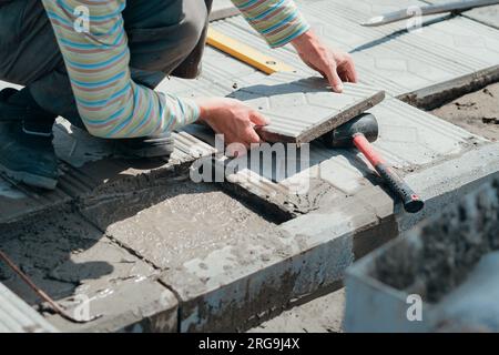 Die Fliesenleger legen an Sommertagen im Freien Fliesen mit Zement. Authentischer Workflow. Hände mit gegenüberliegenden Fliesen. Stockfoto