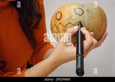 Eine Nahaufnahme von nicht wiedererkennbaren weißen weiblichen Händen mit schwarzem Tintenmarker, einen halloween-Kürbis zeichnen, Kopierraum Stockfoto