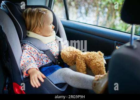 Ein niedliches Kleinkind in einem modernen Autositz mit ihrem Lieblingsspielzeug. Kleines Kind, das mit dem Auto unterwegs ist. Kindersicherheit auf der Straße. Reise mit einem Baby Stockfoto