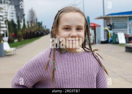 Fröhliches Mädchen mit lächelnden Zöpfen, Outdoor-Porträt Stockfoto