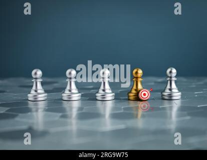 3D Zielpfeil-Symbol auf goldenem Schachfiguren, das in der Gruppe silberner Schachfiguren auf sechseckigem Boden und blauem Hintergrund steht und sich von ihm abhebt Stockfoto