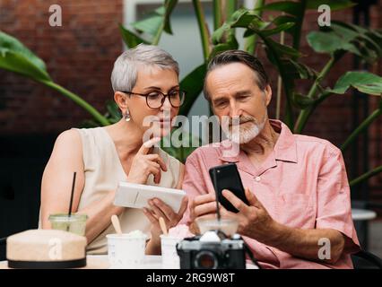 Ältere Ehepaare, die ihre Smartphones benutzen, während sie draußen sitzen Stockfoto