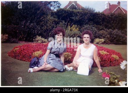 Eine junge Frau und ihre Mutter sitzen auf dem Gras in einem sehr gepflegten formellen Garten mit großen runden BlumenbedenAugust 1963 Stockfoto