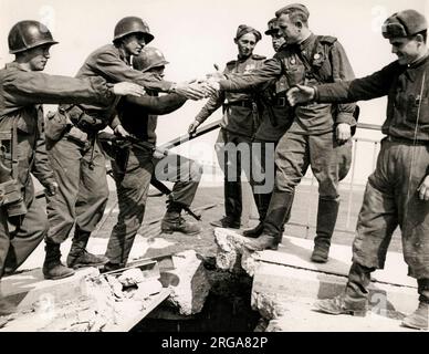 Amerikanische Soldaten der Ersten Armee schütteln sich die Hände mit russischen Kollegen, als sich beide Seiten in Torgau an der Elbe, 1945. Weltkrieg, treffen Stockfoto