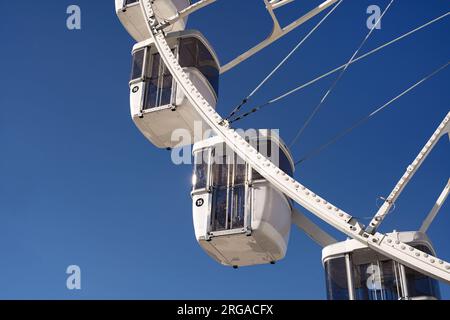 Modernes Riesenrad mit geschlossenen Kabinen auf dem Karneval mit blauem Himmel, keine Wolken im Hintergrund, beleuchtete Weitwinkel-Nahaufnahme Stockfoto