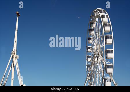 Modernes Riesenrad mit geschlossenen Kabinen auf dem Karneval mit blauem Himmel, keine Wolken im Hintergrund, beleuchtete Weitwinkel-Nahaufnahme Stockfoto