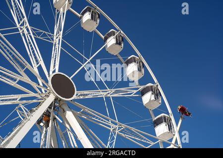 Modernes Riesenrad mit geschlossenen Kabinen auf dem Karneval mit blauem Himmel, keine Wolken im Hintergrund, beleuchtete Weitwinkel-Nahaufnahme Stockfoto