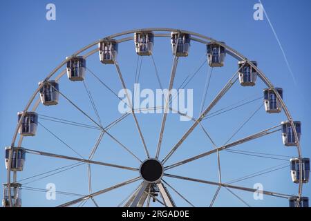 Modernes Riesenrad mit geschlossenen Kabinen auf dem Karneval mit blauem Himmel, keine Wolken im Hintergrund, beleuchtete Weitwinkel-Nahaufnahme Stockfoto