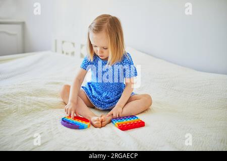 Ein bezauberndes kleines Mädchen, das mit Pop-IT-Fidget spielt. Kind, das mit flexiblem Silikonspielzeug spielt. Entspannung und Anti-Stress-Spielzeuge Stockfoto