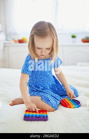 Ein bezauberndes kleines Mädchen, das mit Pop-IT-Fidget spielt. Kind, das mit flexiblem Silikonspielzeug spielt. Entspannung und Anti-Stress-Spielzeuge Stockfoto