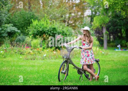 Glückliches junges Mädchen mit Fahrrad und Blumen auf dem Land an einem Sommertag Stockfoto