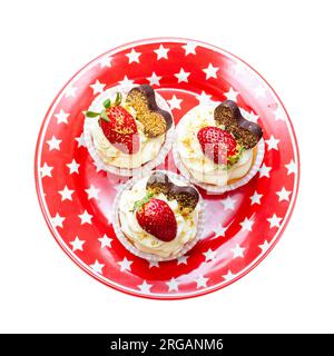 Wunderschöne Vanille-Cupcakes mit Frischkäse-Zuckerguss, dekoriert mit frischen Beeren auf festlichem rotem Teller. Isoliert auf weißem Hintergrund, png Stockfoto
