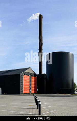 Moderne Fabrik mit einem hohen rostigen Schornstein, aus dem weißer Dampf auf blauem Himmelshintergrund und Schornstein am Himmel austritt Stockfoto