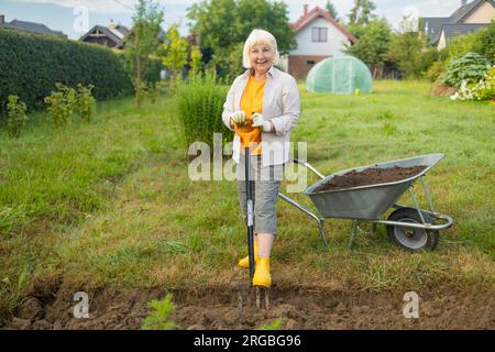 Landwirt, der mit Handwerkzeugen Land im Garten anbaut. Bodenlockerung. Gartenkonzept. Rechen und Spaten auf gelöstem Boden. Landwirtschaftliche Arbeiten Stockfoto