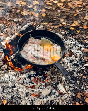 Gebratener Speck und Eier in einer Pfanne über einem Lagerfeuer im Wald Stockfoto