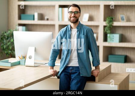 Porträt Eines Gutaussehenden Jungen Geschäftsmanns, Der In Der Nähe Des Schreibtischs In Der Büroeinrichtung Steht Stockfoto