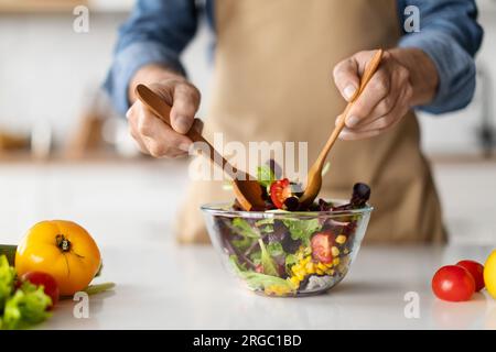 Kochkonzept. Ein unbekannter Mann in der Schürze, der frischen Bio-Gemüsesalat macht Stockfoto