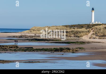 Leute laufen am Weststrand, Lossiemouth mit dem Leuchtturm auf dem Hügel Stockfoto