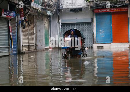 DHAKA, BANGLADESCH - 7. AUGUST 2023: Ein Mann zieht seine Rikscha nach heftigen Regenfällen in Dhaka, Bangladesch am 7. August 2023 durch die überflutete Straße. Stockfoto