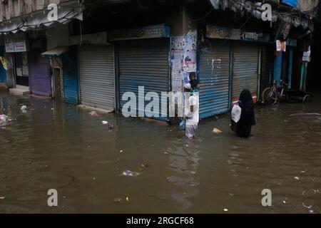 DHAKA, BANGLADESCH - 7. AUGUST 2023: Bewohner gehen nach heftigen Regenfällen in Dhaka, Bangladesch am 7. August 2023 durch die überflutete Straße. Stockfoto