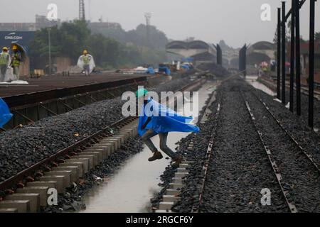 DHAKA, BANGLADESCH - 7. AUGUST 2023: Ein Arbeiter bedeckt sich mit einem Stück Polyethylen, während er bei Regenfällen in Dhaka, Bangladesch, am 7. August 2023 die Bahngleise überquert. Stockfoto