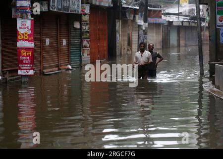 DHAKA, BANGLADESCH - 7. AUGUST 2023: Bewohner gehen nach heftigen Regenfällen in Dhaka, Bangladesch am 7. August 2023 durch die überflutete Straße. Stockfoto