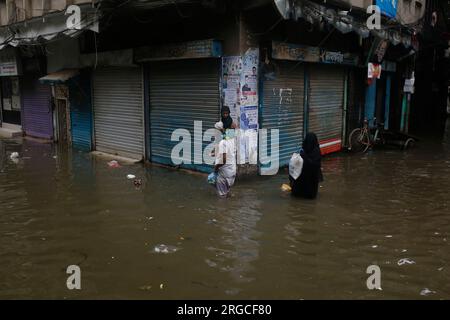 DHAKA, BANGLADESCH - 7. AUGUST 2023: Bewohner gehen nach heftigen Regenfällen in Dhaka, Bangladesch am 7. August 2023 durch die überflutete Straße. Stockfoto