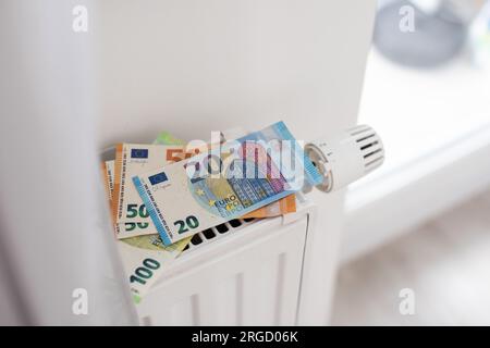 Neuer Thermostat mit Euro-Bargeld auf einer Heizkörperheizung zu Hause. Teure Heizkosten symbolisches Image. Stockfoto