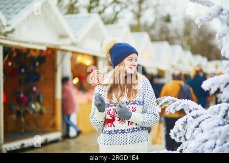 Glückliche junge Frau auf dem Weihnachtsmarkt in Paris, Frankreich. Ein Mädchen, das Lutscher isst. Aktivitäten im Freien an Weihnachten und Neujahr Stockfoto