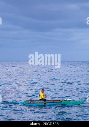 Dumaguete, Negros Island, Philippinen-Februar 01 2023: Mit einer Schutzbrille wirft der Mann relativ große Netze und taucht für Fische in der Dämmerung ins Wasser. Stockfoto