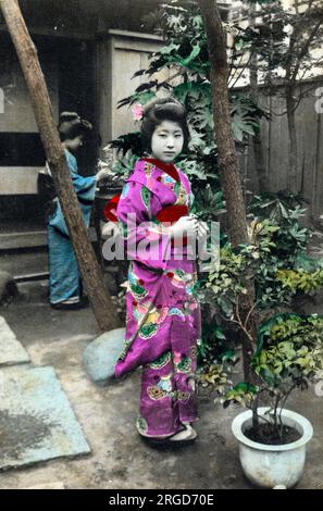 Junge Japanerin in einem traditionellen Garten, trägt einen lila und pinkfarbenen Kimono. Stockfoto