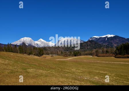 Blick auf den schneebedeckten Gipfel von Kocna und Grintovec in den Kamnik-Savinja-alpen und waldbedeckte Hügel und Felder vor dem Hotel Stockfoto