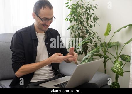 Junger Mann, der Gesten in Gebärdensprache zeigt, mit dem Laptop Videoanrufe führt Stockfoto
