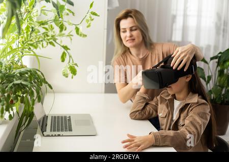 Familien und neue Technologien. Lächelnde Arbeit-zu-Hause-Mutter, die mit ihrer Tochter einen VR-Helm trägt und die virtuelle Realität erforscht. Neugieriges Teenager-Mädchen Stockfoto