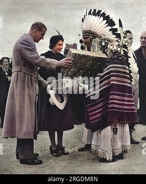 In Winnipeg erhalten Prinzessin Elizabeth und Prinz Philip während der königlichen Rundfahrt durch Kanada ein Geschenk für Prinzessin Anne. Das Geschenk ist ein kleiner indianischer Anzug, hergestellt von Mrs. Antoinette Heavyshield, der hier im Namen aller Mütter aller fünf indianischen Völker im Süden Albertas gesehen wird. In der Mitte ist Chief Percy Creighton, der als Dolmetscher fungiert. Stockfoto