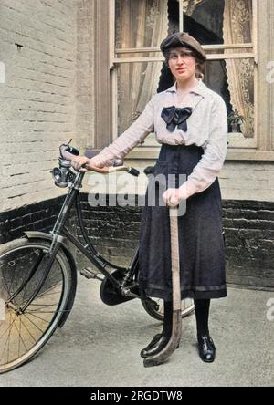 Eine junge Frau mit einem Fahrrad und einem Hockeyschläger, die vor einem Fenster steht. Stockfoto