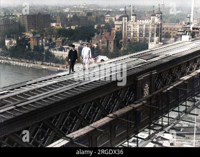 Zwei Männer in Anzügen stehen auf einem der Gehwege über die Tower Bridge in London. Der Tower of London ist im Hintergrund zu sehen. Stockfoto