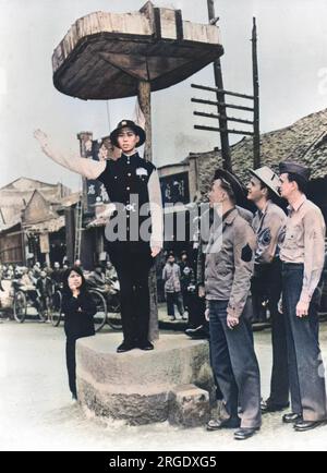 Amerikanische Soldaten beobachten einen chinesischen Polizisten, der den Verkehr irgendwo in China lenkt, in einer Stadt in der Nähe einer US-Militärbasis Stockfoto