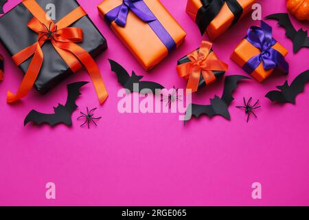 Komposition mit Geschenkboxen, Spinnen und Fledermäusen für Halloween auf pinkfarbenem Hintergrund Stockfoto